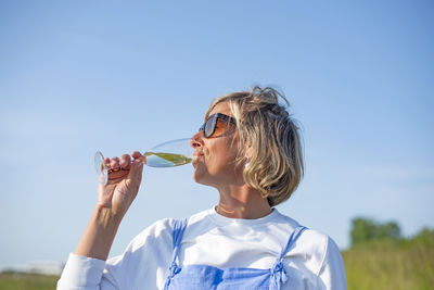 Portrait of woman holding sunglasses against sky