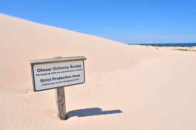 Information sign on sand dune in desert against blue sky