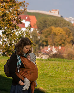 Side view of woman with baby carrying in fabric on field