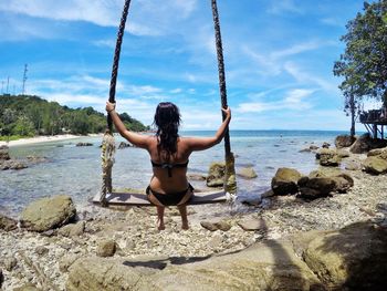 Rear view of woman sitting on rock against sea