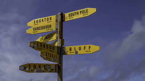 Low angle view of direction sign against sky with distances to far off cities
