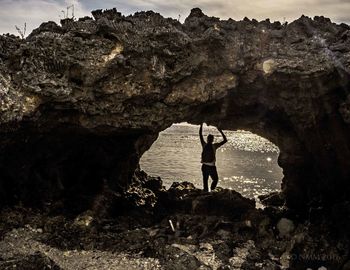 Rear view of man standing below natural arch against sea