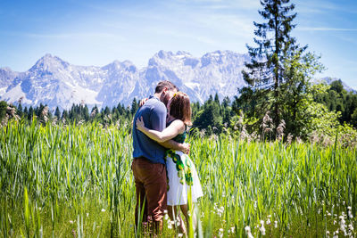 Rear view of friends standing on field against mountains