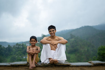 Portrait of friends sitting on rock against sky