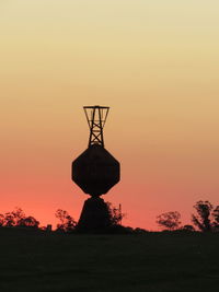 Silhouette cranes on field against sky during sunset