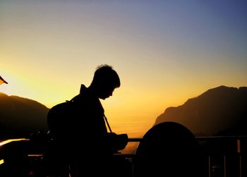 Silhouette man sitting against orange sky during sunset