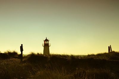 Silhouette of lighthouse on field against clear sky