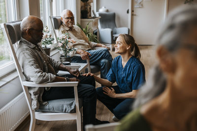 Smiling nurse talking with elderly man sitting on chair at care home