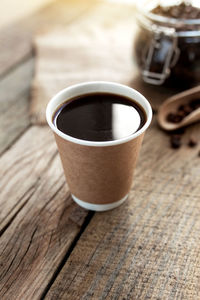 Paper cup of black coffee espresso, dry roasted coffee beans and spoon at old wooden table