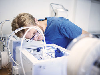 Technician wearing eyeglasses analyzing 3d printer at workshop