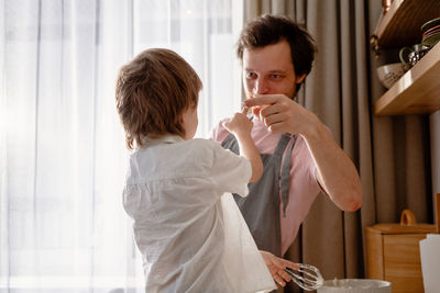 Dad holds a blender and plays with his little son. rubs his nose with whipped cream