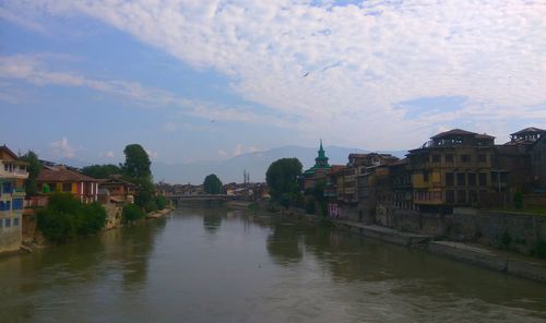 Buildings by river against sky in town