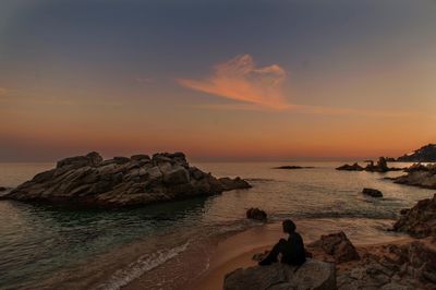 Rear view of woman standing on beach against sky during sunset