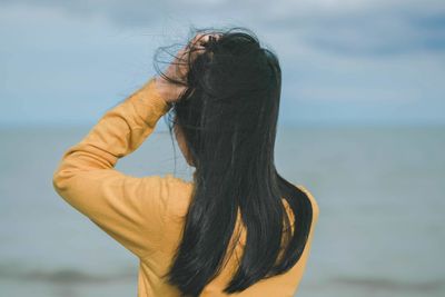 Close-up of woman with hand in hair against sea