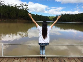 Rear view of woman standing by lake against sky