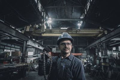 Male worker carrying work tool looking away while standing in factory