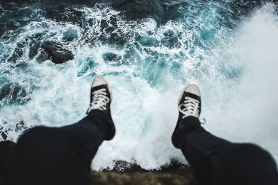 Low section of man sitting on cliff over sea