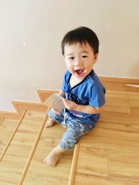Portrait of cute boy sitting on wooden floor at home