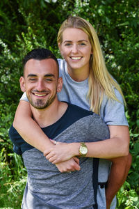 Portrait of happy young man piggybacking girlfriend at park