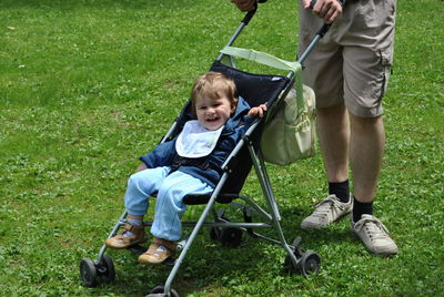 Low section of father with cute son in baby stroller standing on field