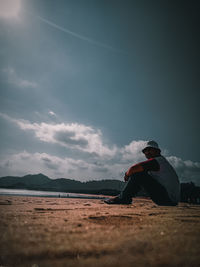 Man sitting on land against sky