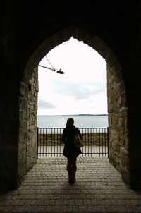 Rear view of woman standing in balcony of historic building against cloudy sky