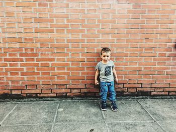 Full length portrait of boy standing against brick wall