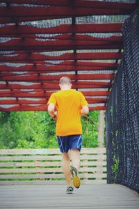 Rear view of man jogging on footbridge