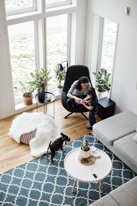 High angle view of mother showing mobile phone to daughter while dog on floor at home