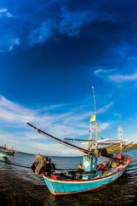 Fishing boats moored on sea against blue sky