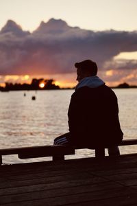 Rear view of man sitting on shore against sunset sky