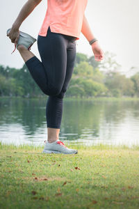 Low section of woman standing on grass by lake