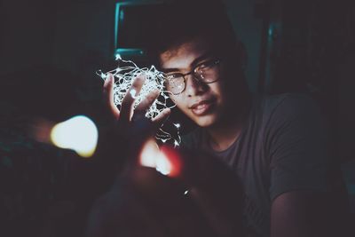 Portrait of man holding illuminated string lights in darkroom