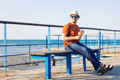 Man sitting on railing against sea
