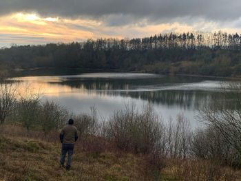Rear view of man standing by lake against sky