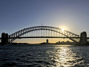 Silhouette bridge over river against clear sky during sunset
