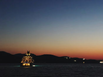 Illuminated ship sailing in sea against sky during sunset