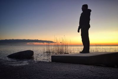 Silhouette man standing at kalmar strait against sky during sunset