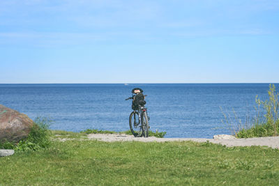 Man riding bicycle by sea against sky
