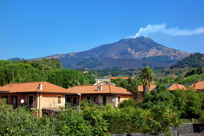 Houses and trees by mountains against blue sky