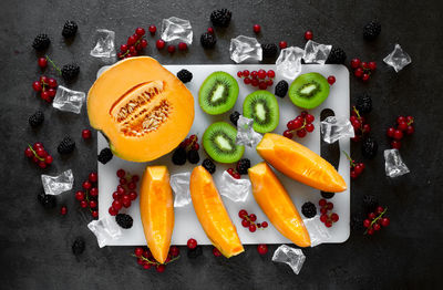 Top view cutting board with fresh fruit on dark gray background with cold water drops and ice cubes