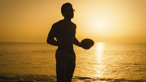 Silhouette of a boy playing american football at dawn in the calm ocean