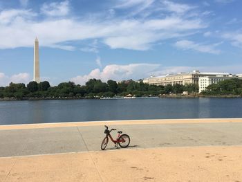 Bicycle by river in city against sky