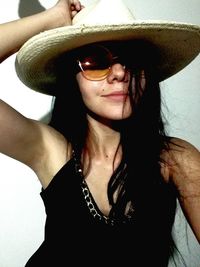 Close-up portrait of young woman wearing sunglasses and sun hat against wall