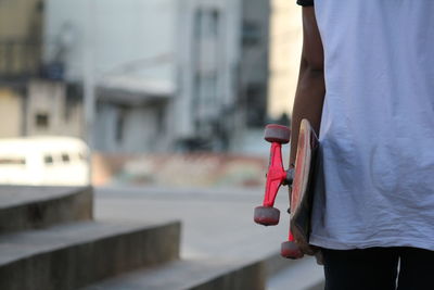 Midsection of girl carrying skateboard at park