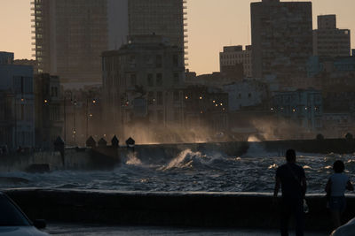 People standing on promenade by sea against buildings in city