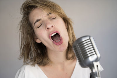 Close-up of woman singing against colored background