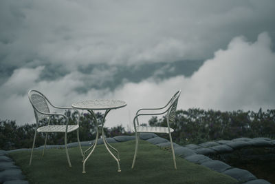 Empty chairs on field against sky