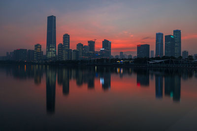 Reflection of buildings in city against sky during sunset