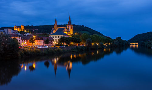 Reflection of illuminated buildings in lake against blue sky